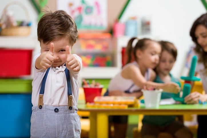 dziecko pokazujacy kcuiki do gory w przedszkolu